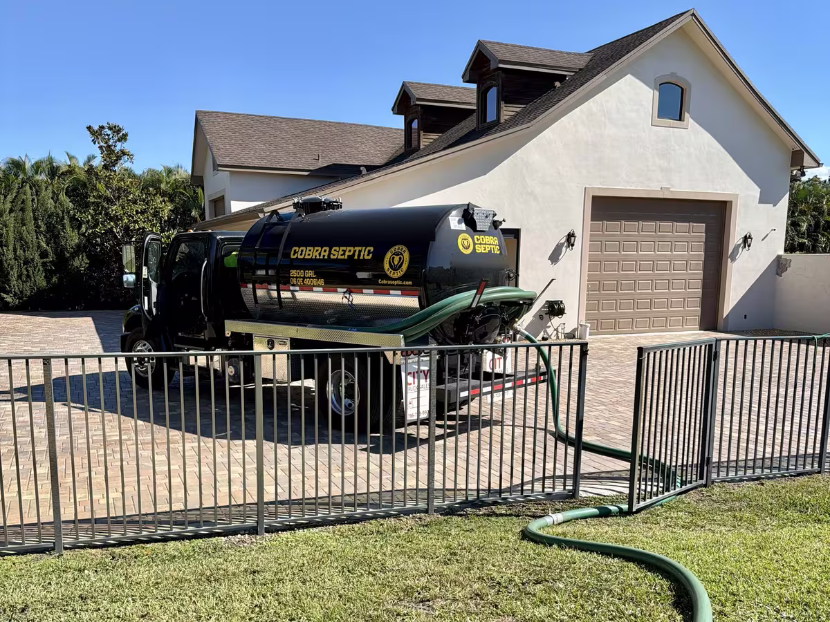 A suction hose run from a Cobra Septic truck across a driveway to a tank
